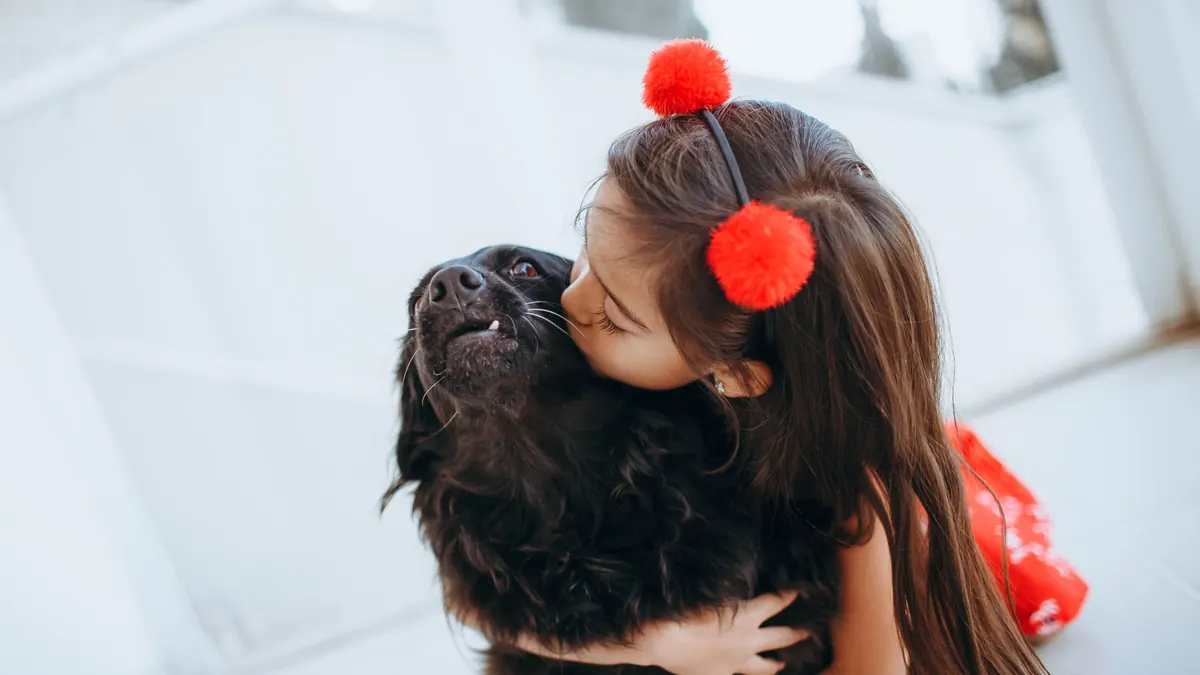 Menina abraçando e beijando um cachorro preto em casa