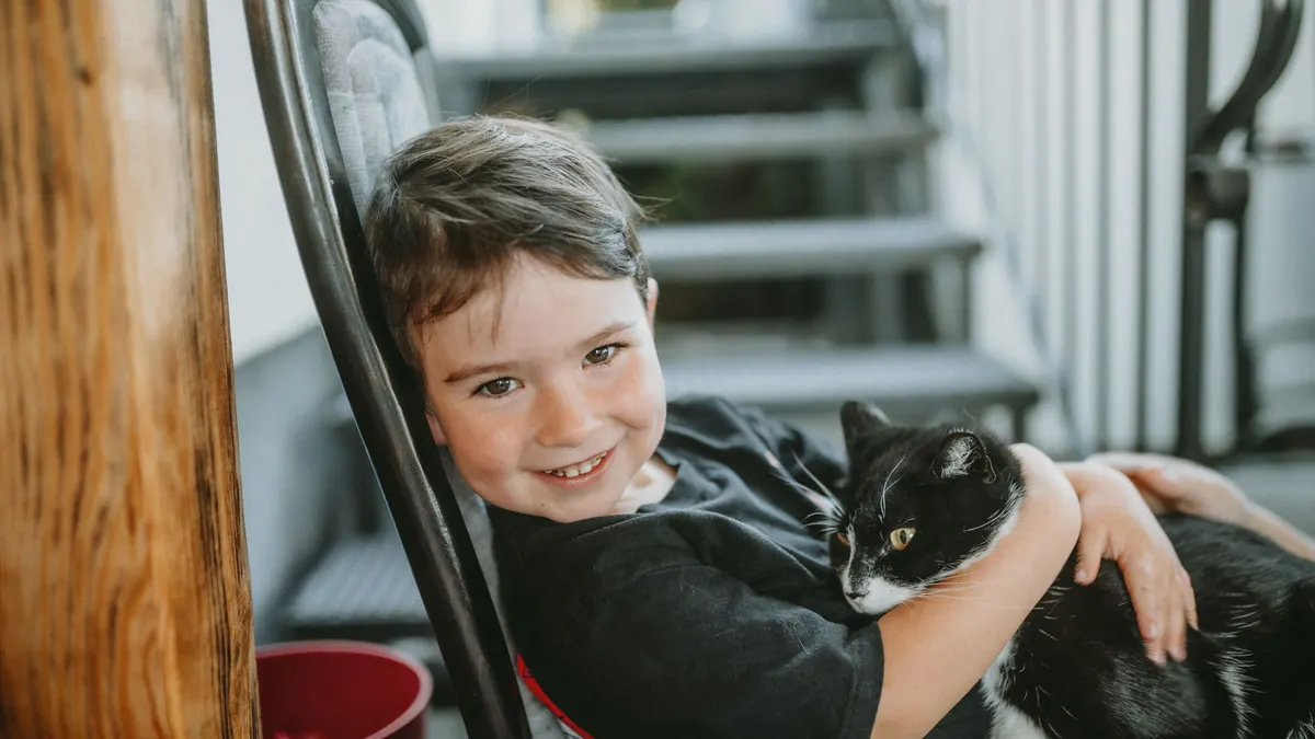 Menino sorrindo e abraçando um gato preto e branco em casa