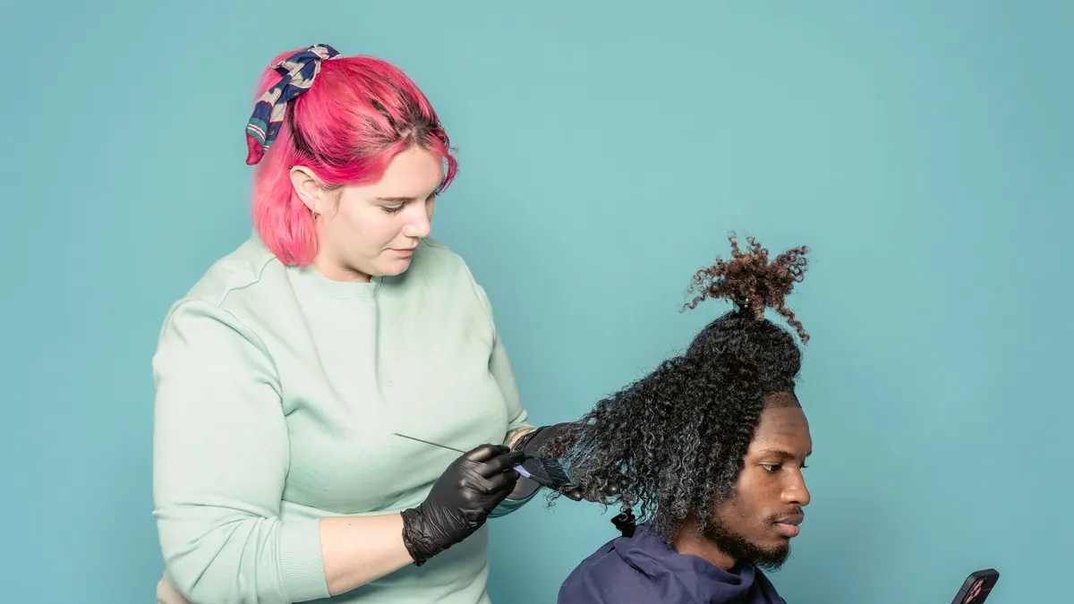 Cabeleireira de luvas pretas passando tintura no cabelo cacheado de um homem