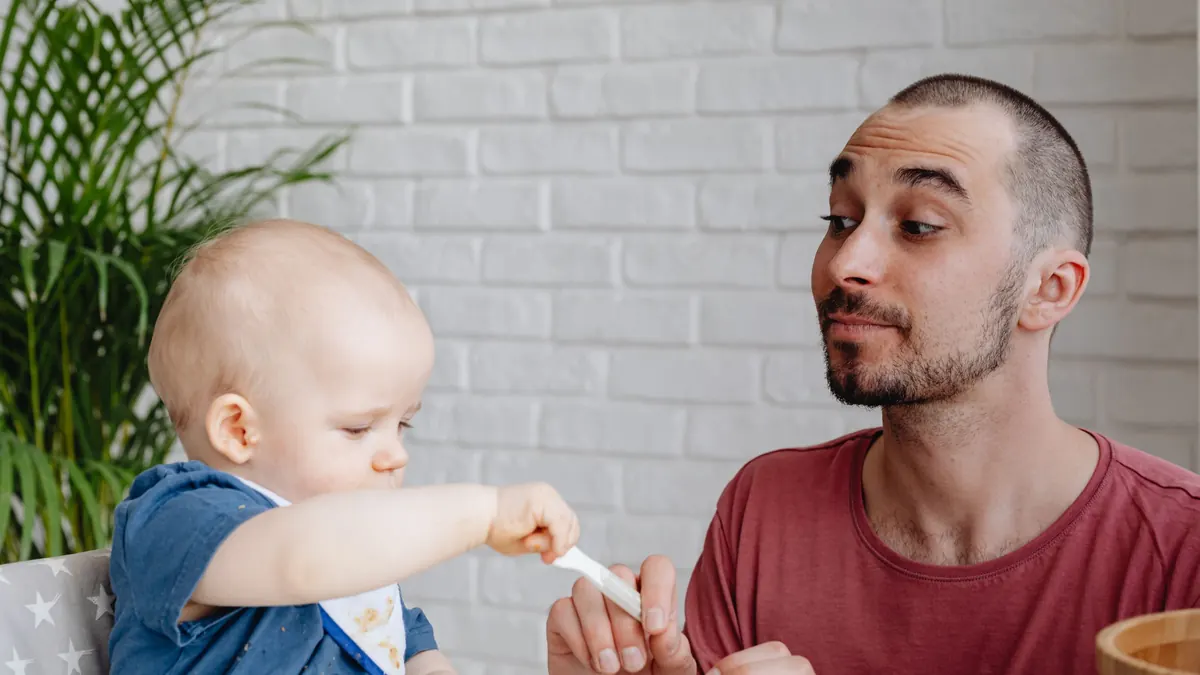 Pai sentado à mesa ajudando o bebê a comer