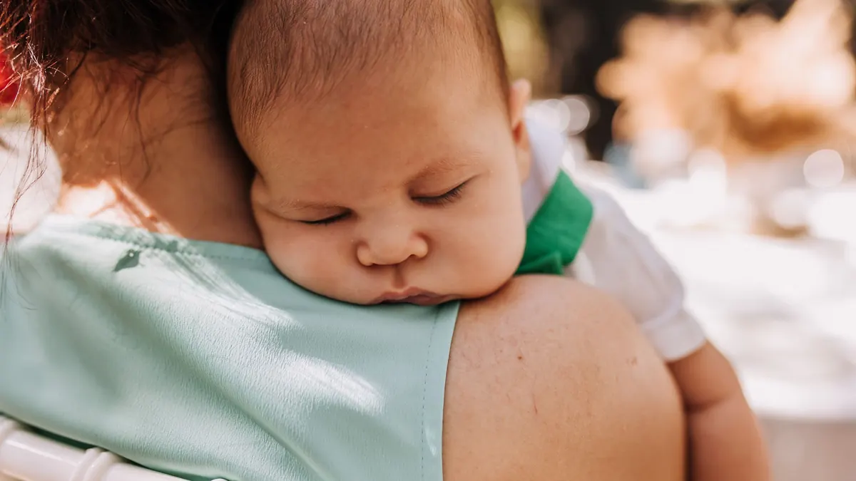 Bebê dormindo no ombro da mãe, no colo, em pé