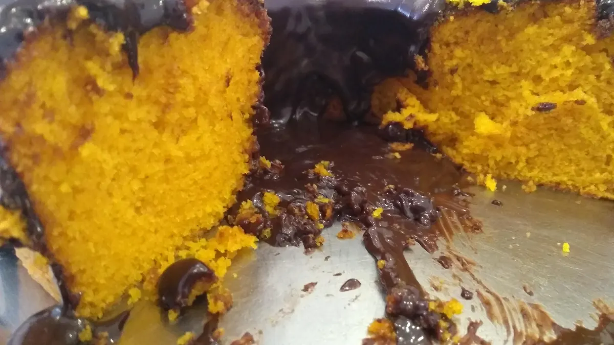 Bolo de cenoura cortado, com o miolo laranja e fofinho e cobertura de chocolate