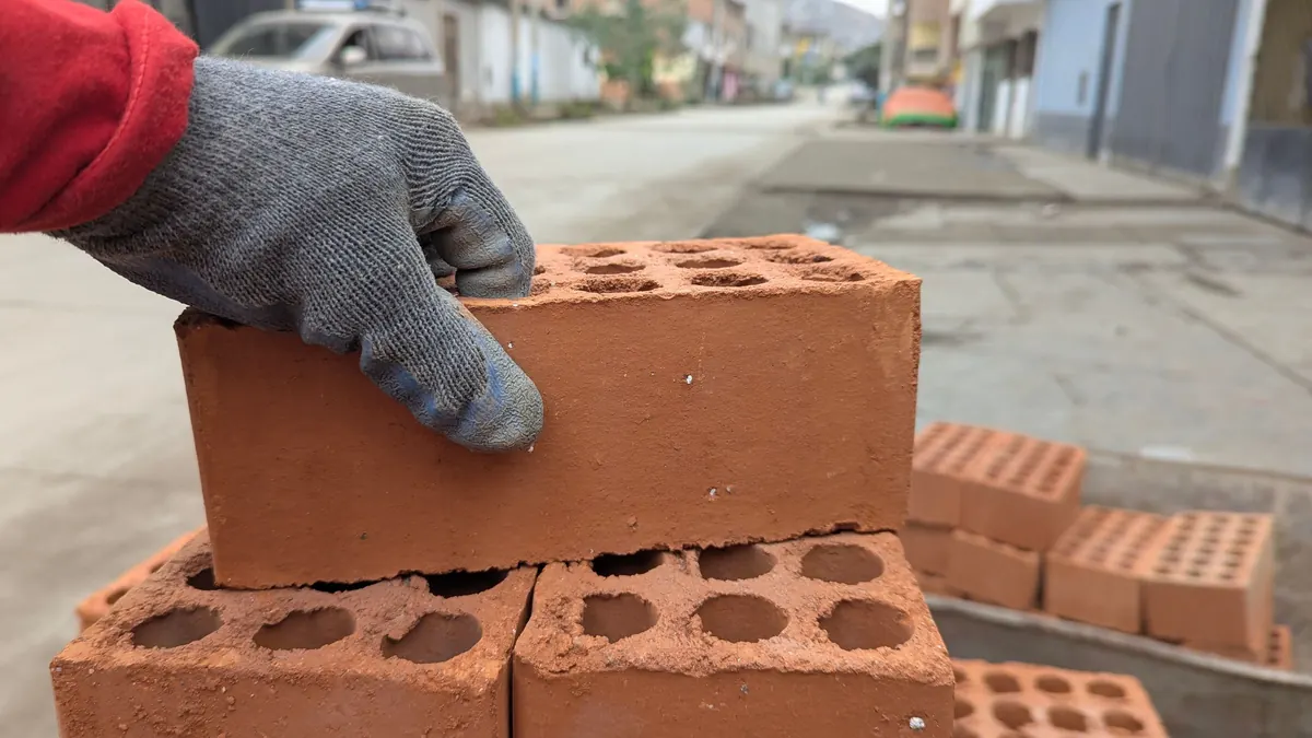Mão com luva de trabalho apoiando um tijolo numa obra de rua
