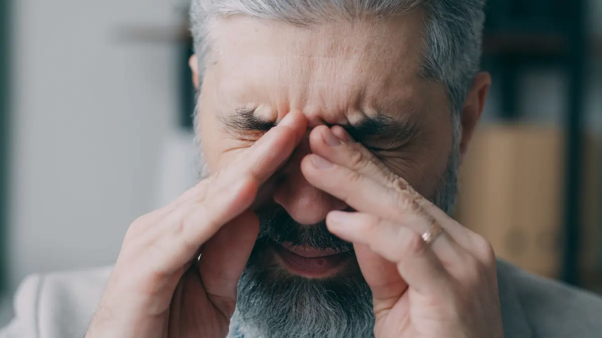 Homem de barba grisalha esfregando os olhos com as duas mãos