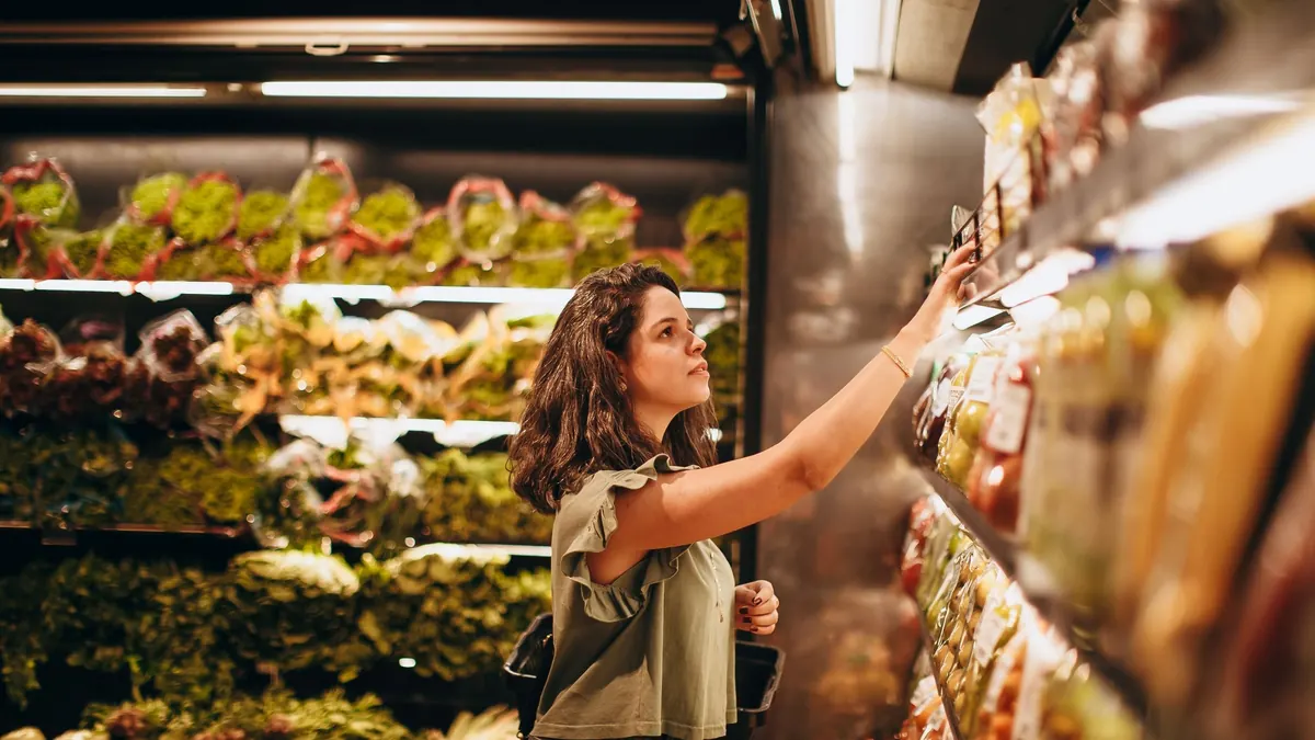 Mulher no corredor do supermercado pegando um produto na prateleira