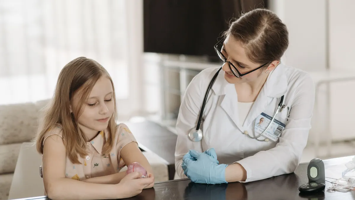 Médica conversando com uma menina sentada à mesa do consultório