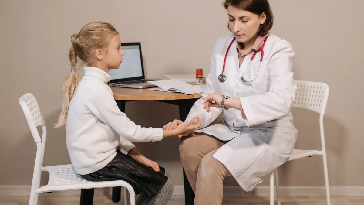 Médica examinando uma menina sentada à mesa do consultório