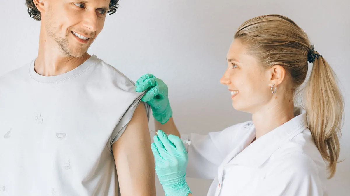 Profissional de saúde aplicando injeção no braço de um homem sorridente