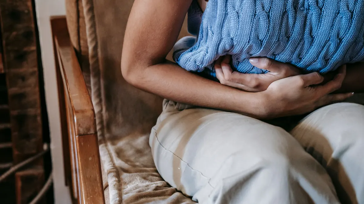 Pessoa sentada numa poltrona, abraçando uma almofada contra a barriga, com desconforto