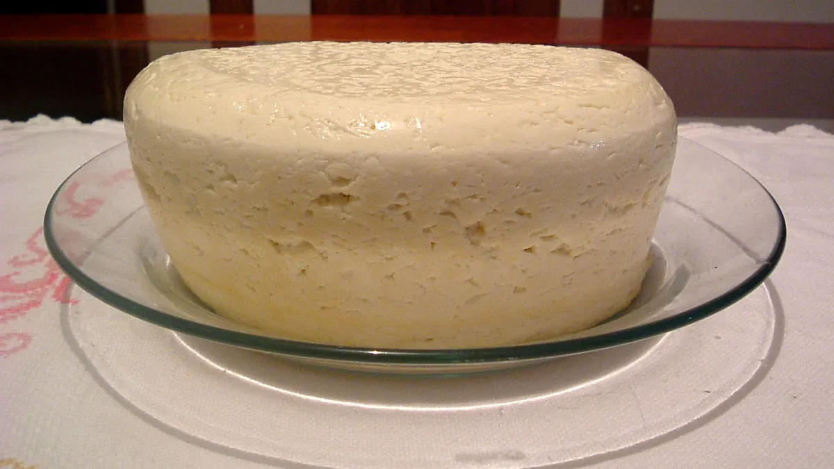 Queijo minas frescal inteiro num prato de vidro, sobre toalha bordada
