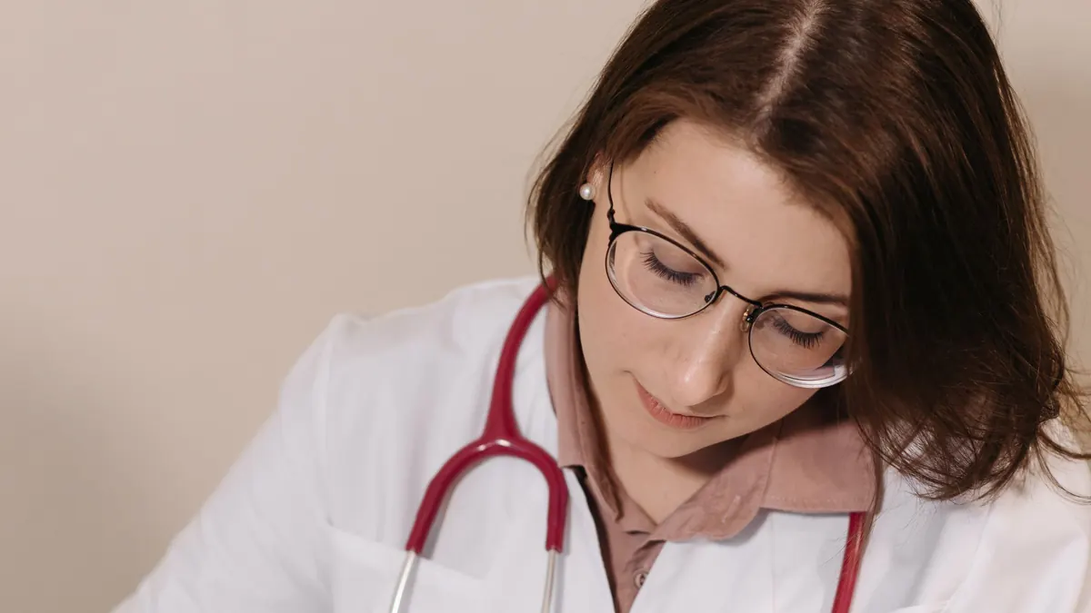 Médica de jaleco e estetoscópio escrevendo uma receita no consultório