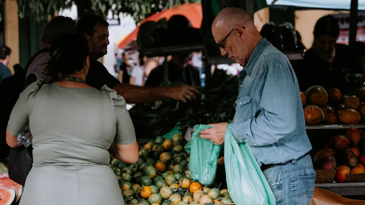 Pessoas escolhendo frutas e carregando sacolas plásticas numa feira livre