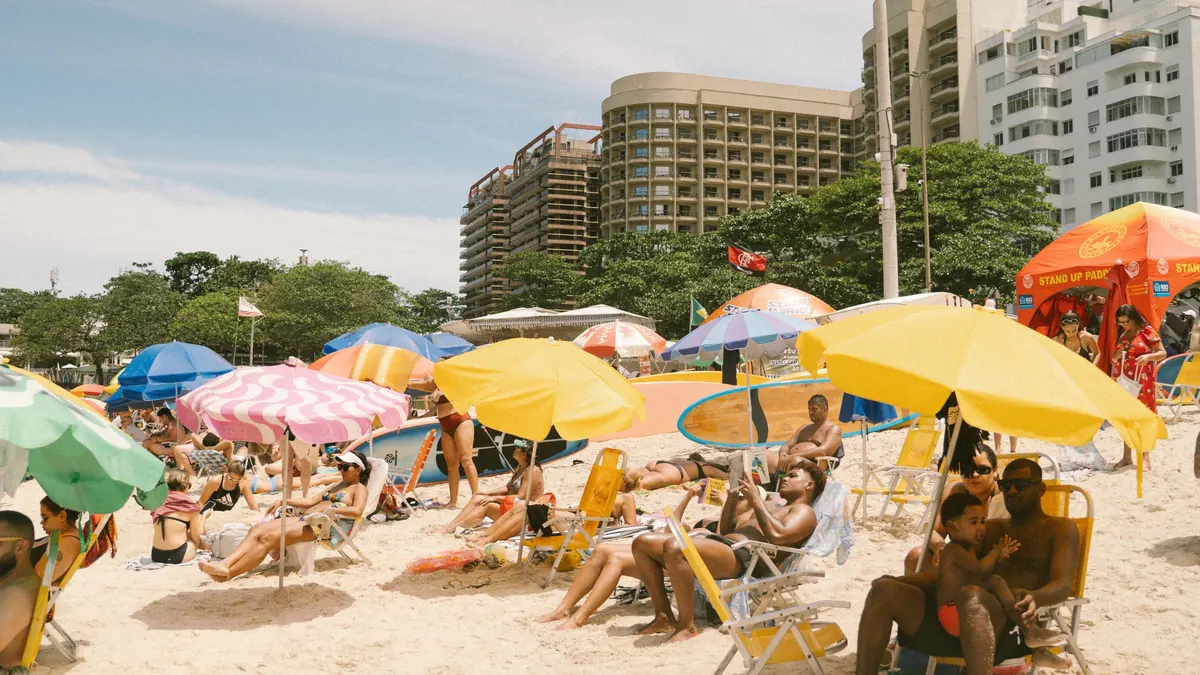 Praia brasileira cheia num dia de sol, com guarda-sóis coloridos e prédios ao fundo
